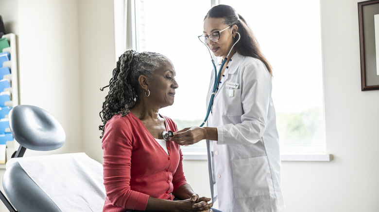Doctor listening to senior woman's heart in exam room