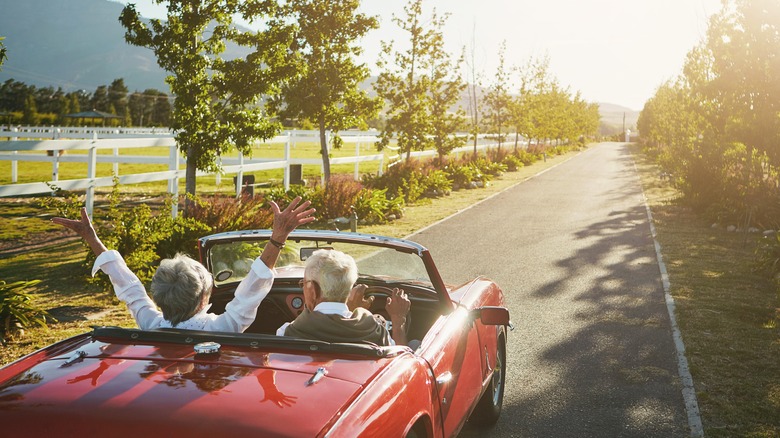 Older couple driving down the road in a car in evening sunlight.