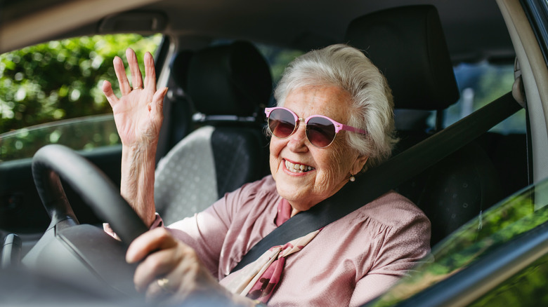 elderly woman wearing pink rimmed sunglasses driving a car