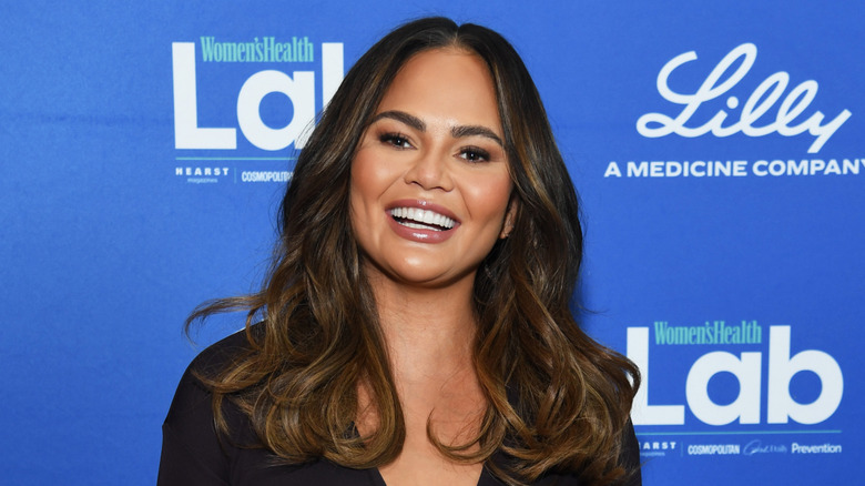 Model Chrissy Teigen smiles as she poses in front of blue back drop