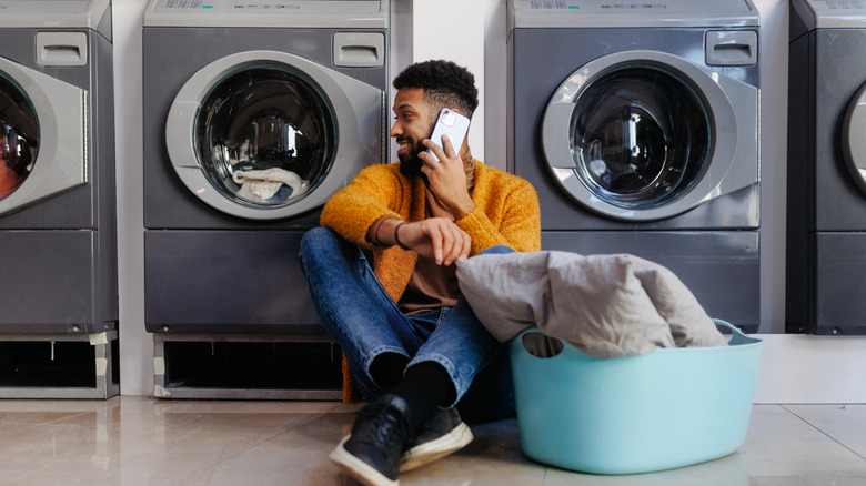 Young multiracial man in laundry, sitting on the floor, calling and waiting.