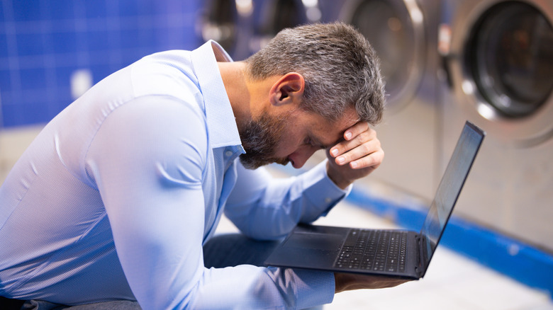 A man doing laundry while working on laptop.