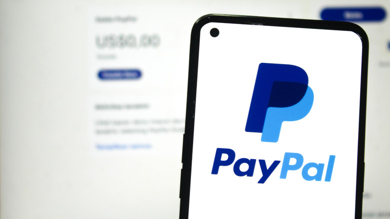 PayPal logo on phone screen with PayPal account website in the background