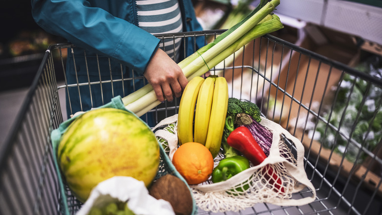 A hand places fresh produce into a shopping cart at a grocery store