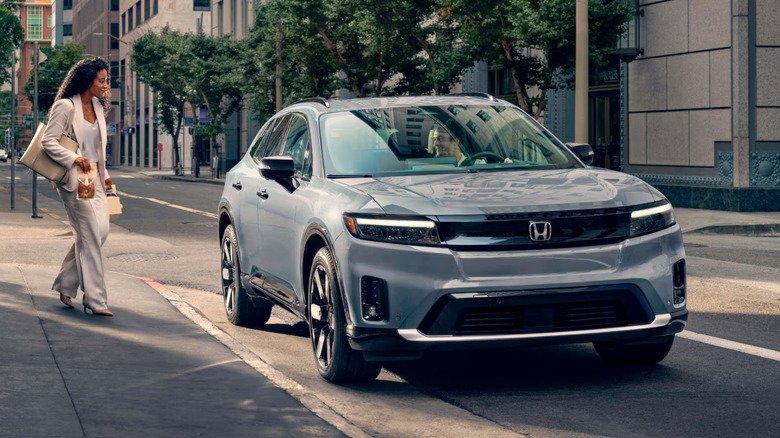well-dressed woman in white carrying snacks approaches blue-gray Honda Prologue