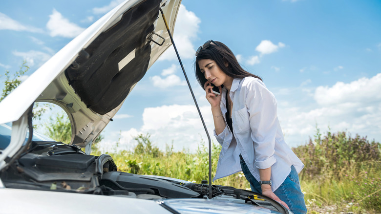 Woman looking under the hood of a broken-down car