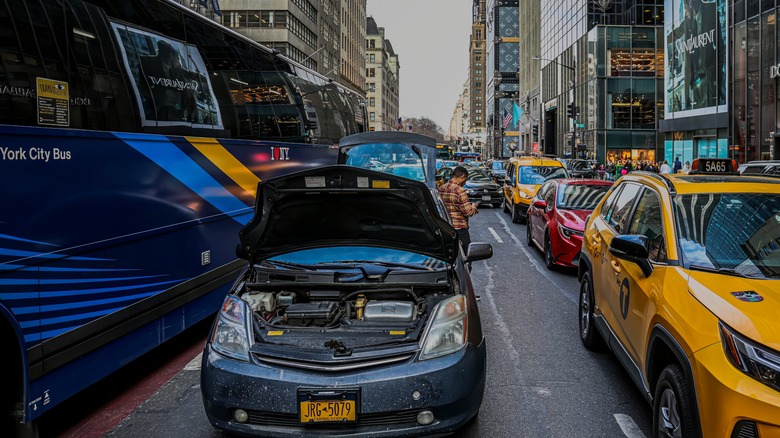 A stalled vehicle with its hood raised blocking traffic in New York City.