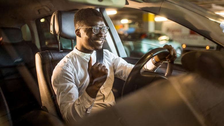 A smiling Gen Z professional behind the wheel of their car celebrating good news.