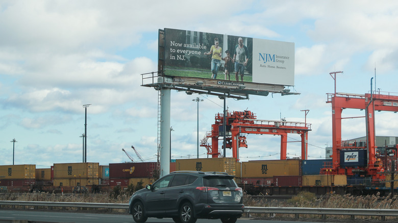 A billboard advertising NJM Insurance Group in New Jersey is located along a road near railroad tracks.