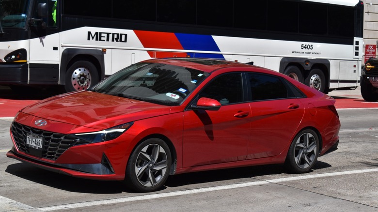 Red 2025 Hyundai Elantra Hybrid driving on the road next to a Metro bus