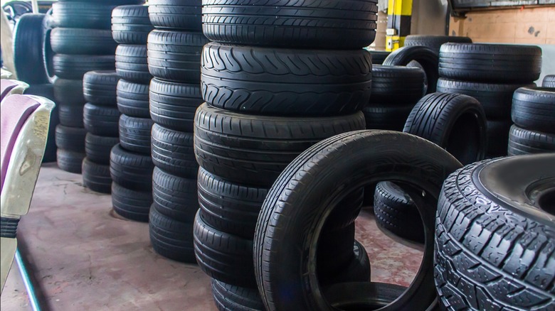 Stacks of car tires piled in a garage or tire shop, with various tread patterns visible