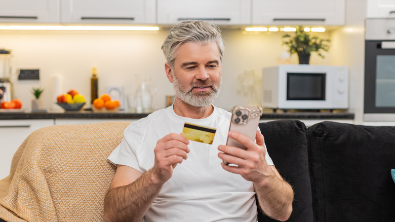 A middle aged man holding his credit card and smartphone.