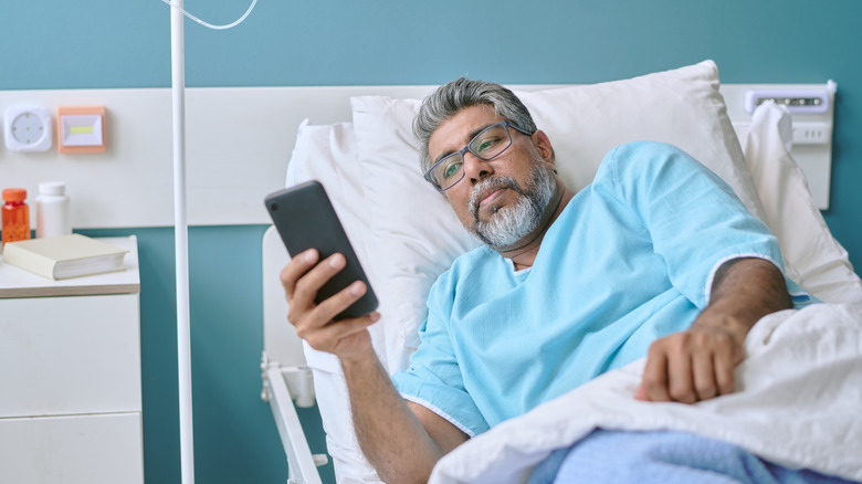 A middle aged man lying in hospital bed using smartphone.
