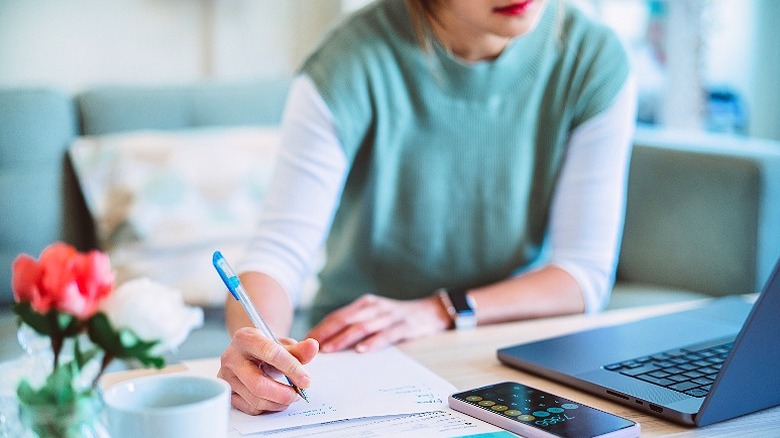 Woman budgeting at home with pen and paper, a laptop, and a smartphone