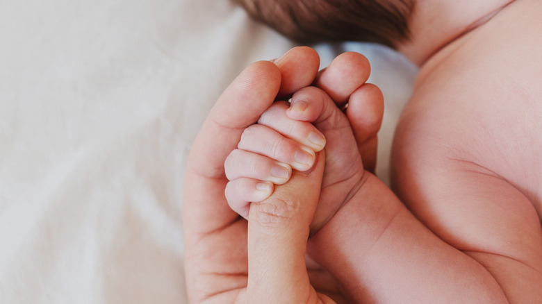 Photo of a baby's arm with fingers wrapped around a grown up's finger