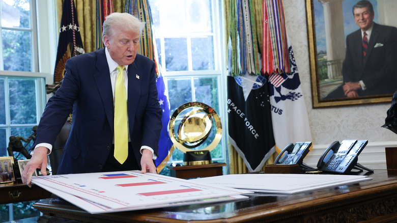 Trump shuffling charts on his resolute desk in the White House's Oval Office.