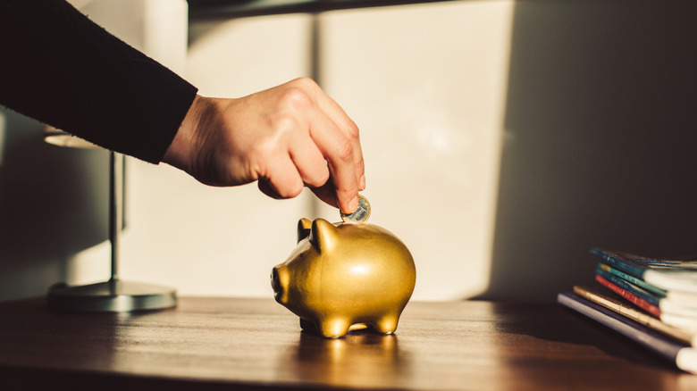 Person inserting a coin into a piggy bank