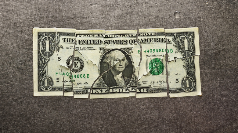 A one dollar bill shown torn into many pieces