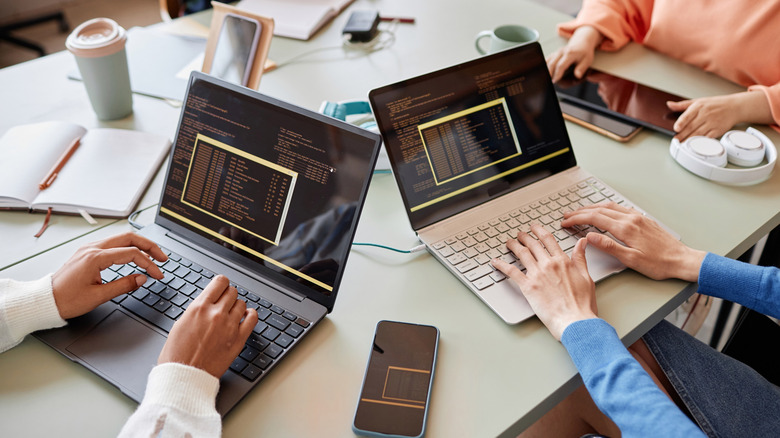 A group of anonymous people sitting at a table and typing on laptops