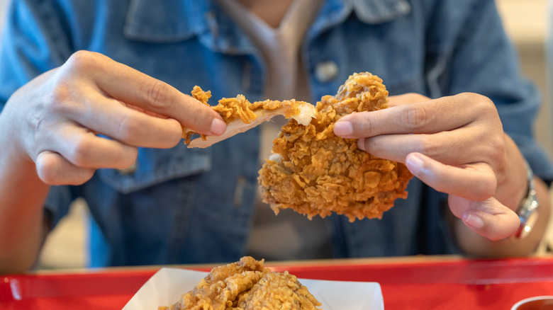 A young woman eating fried chicken on a plastric tray
