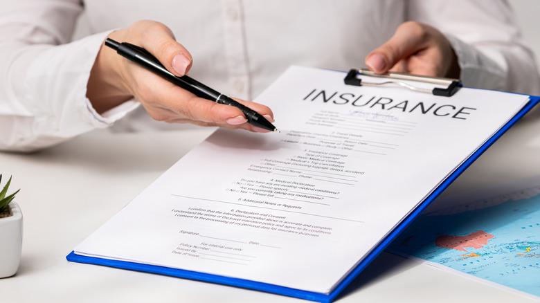 Woman gestures to clipboard with paper that has insurance written at top while holding pen