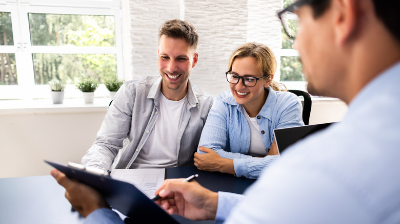 Smiling couple look down at a clipboard held by man wearing glasses