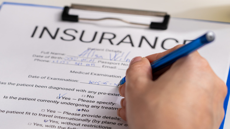 a hand holding a blue pen and filling out an insurance form