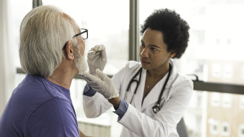 Female doctor checking the throat of an older man