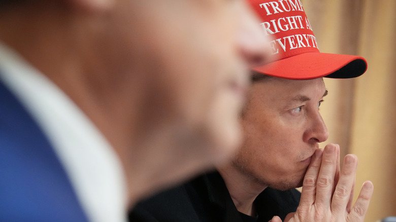 Elon Musk sitting next to Trump wearing a MAGA hat