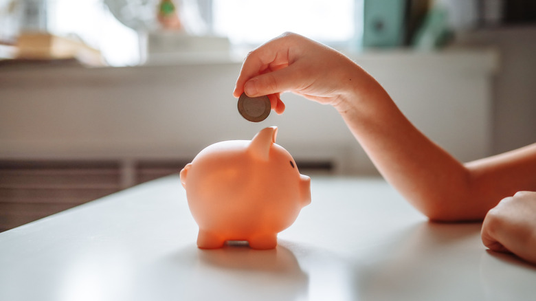 Person adding coin to piggy bank.
