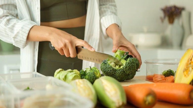 Women chops broccoli with other vegetables in front