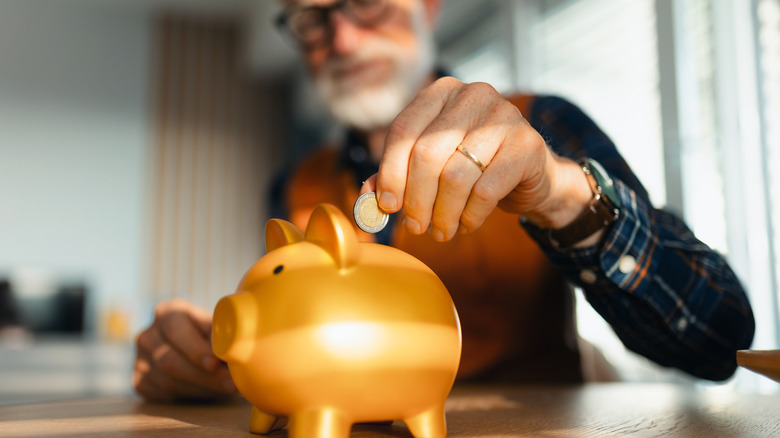 retired man putting coin in golden piggy bank