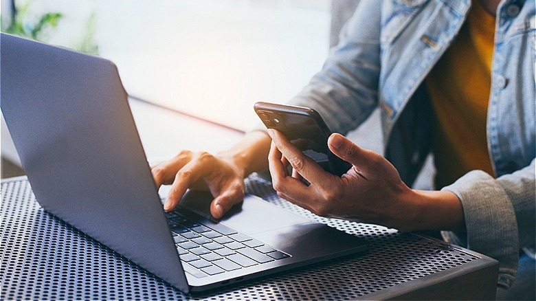 Person holding smartphone, using computer