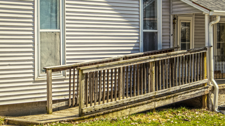 An aging tan home with an old wooden wheelchair ramp.