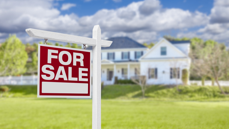 For sale sign with a large home in the background