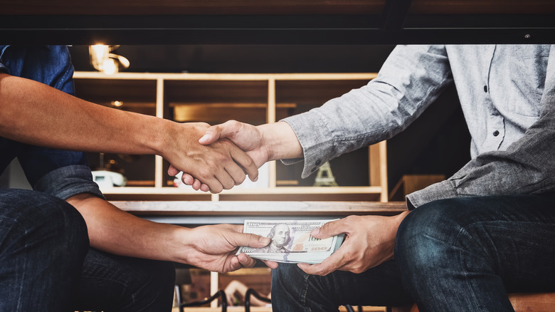 A man handing money to someone under a table