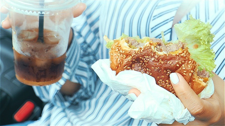 Person holding soda, half-eaten burger