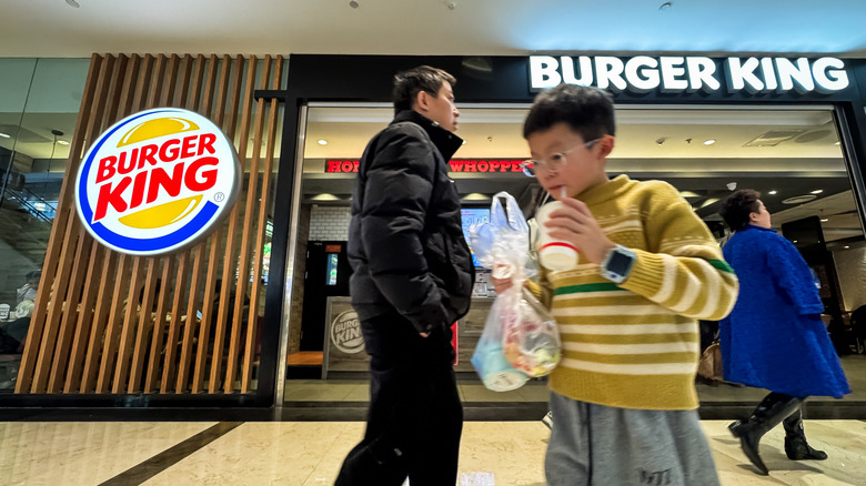 A child drinks a beverage while carrying a takeaway bag outside a Burger King restaurant