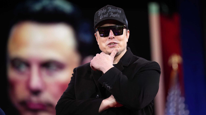 Elon Musk wearing a black Make America Great Again hat and sunglasses.