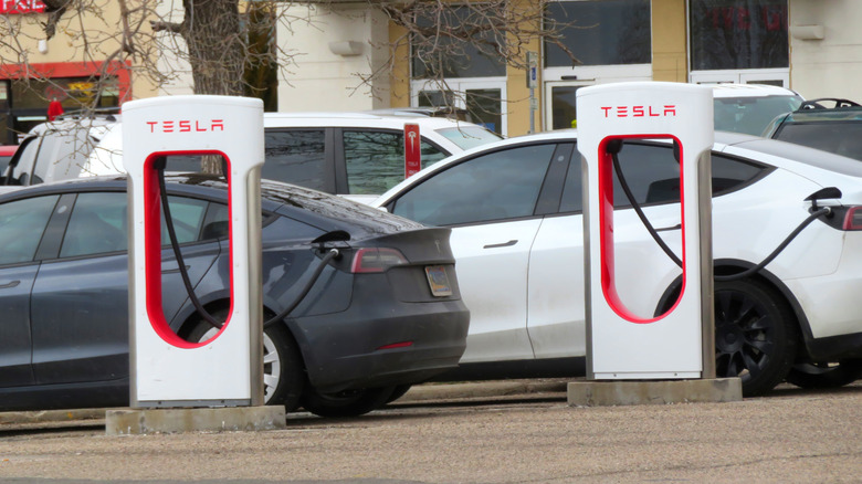 Two Teslas charge side-by-side in a shopping center parking lot.