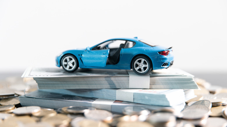 Car figurine stacked on a pile of cash and coins.