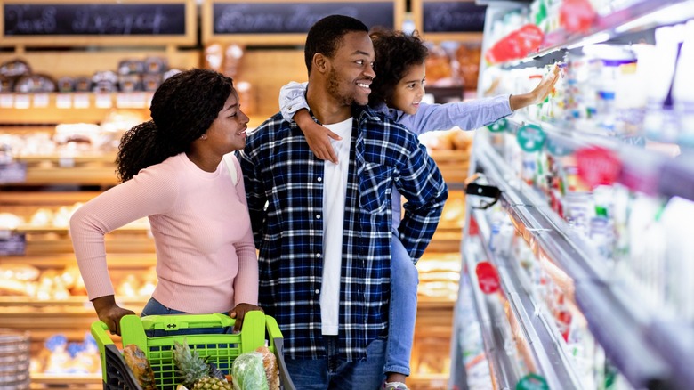A family shopping with the girl on her father's back reaching out to grab something off the shelf