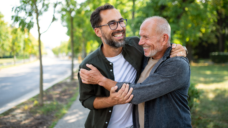 Happy senior father meeting and hugging with his adult son outdoors in park.