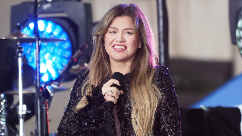 Kelly Clarkson smiling while holding a microphone