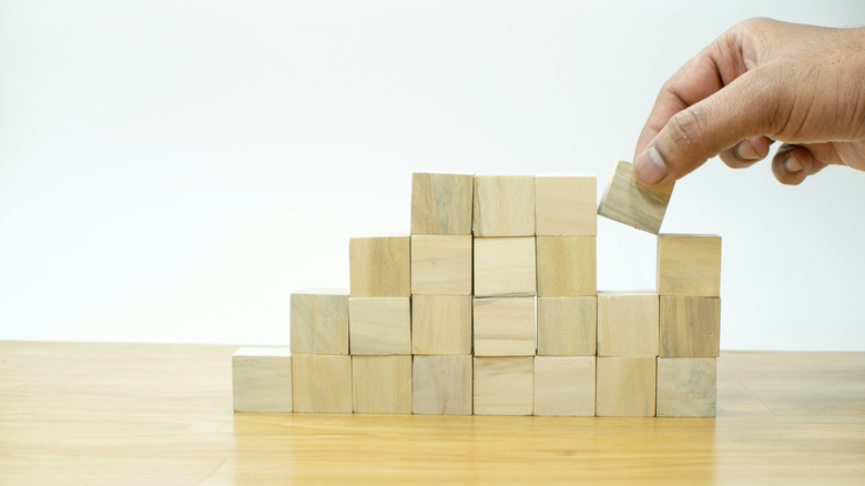 A person placing a block into a pile of wooden blocks