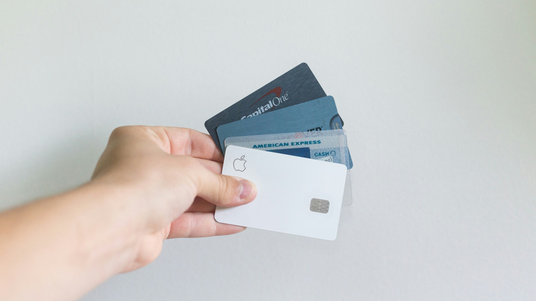 person holding four credit cards against a white background wall.