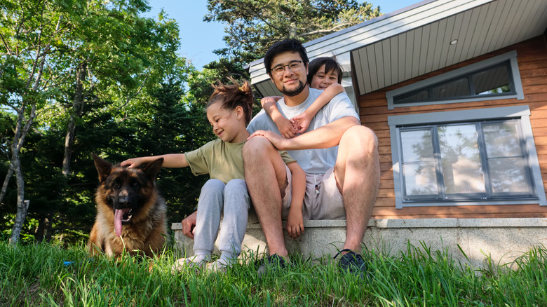 A family with a father and two children on the lawn near their house.