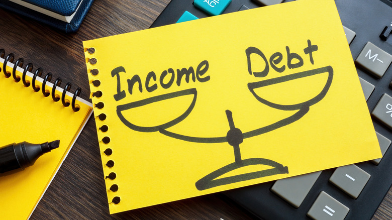 The words income and debt written on a notepad over a scale
