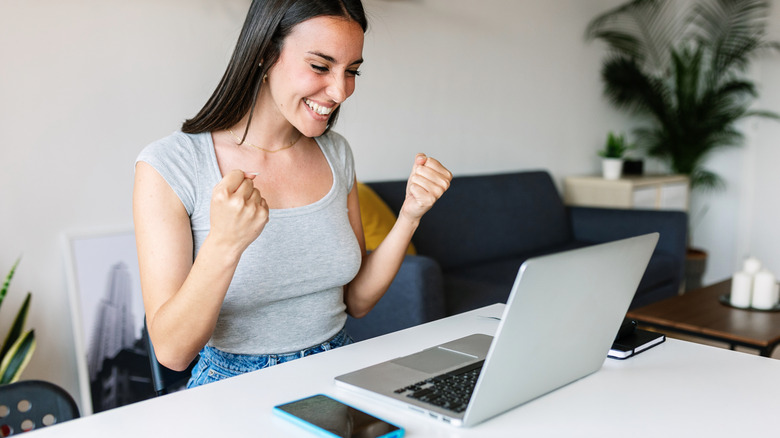 A woman looking triumphant in front of laptop computer.