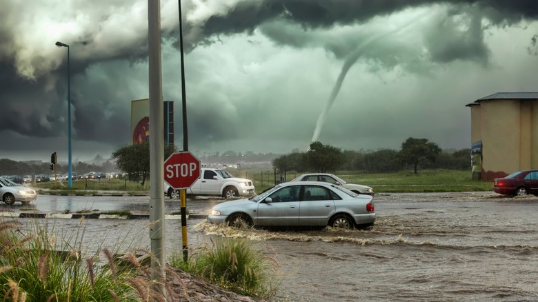 Vehicles driving through flooded streets with a tornado in the background